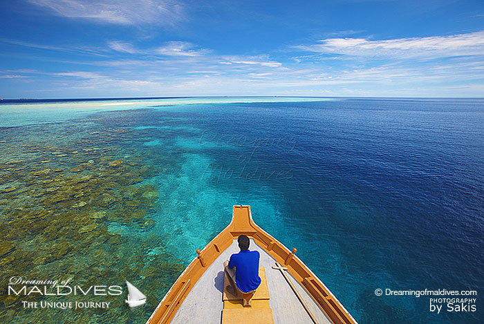 membre d’équipage assis à la proue d'un dhoni, aide le capitaine à se faufiler entre les récifs en observant avec attention la mer pour éviter les coraux.